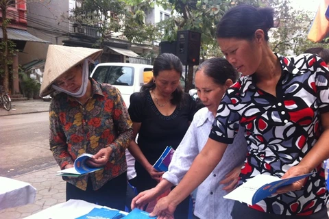Nữ lao động di cư tại chợ Long Biên, Hà Nội đang xem tài liệu tư vấn về sức khỏe, pháp luật. (Ảnh: Hồng Kiều/Vietnam+)