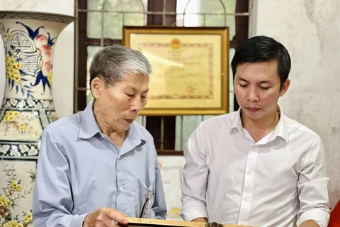 Ông Nguyễn Hữu Luyên cùng con trai ôn lại truyền thống vẻ vang của các liệt sỹ, Bà mẹ Việt Nam anh hùng trong gia đình. (Ảnh: PV/Vietnam+)