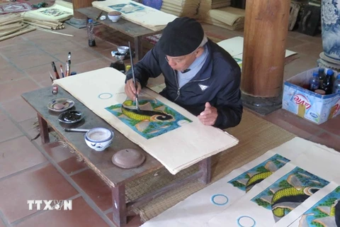 Nghệ nhân Nguyễn Đăng Chế hoàn thiện bức tranh "Cá chép trông trăng." (Ảnh: TTXVN)