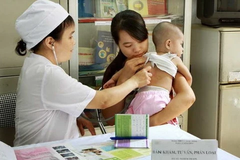 Nhân viên y tế khám sàng lọc sức khỏe cho trẻ trước khi tiêm. (Ảnh: Dương Ngọc/TTXVN)