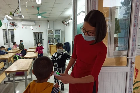 Giáo viên thực hiện đo thân nhiệt cho học sinh trước khi vào lớp. (Ảnh: Phạm Mai/Vietnam+)