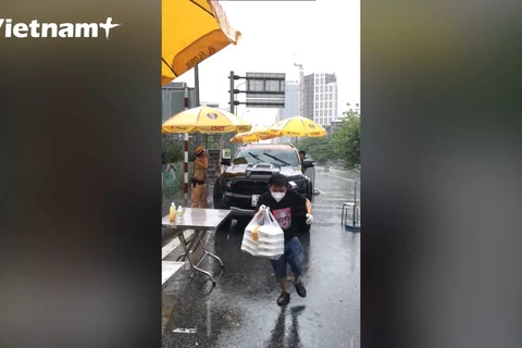 Người dân tiếp đồ ăn cho các cán bộ trực chốt dưới mưa. (Ảnh: Hoàng Đạt/Vietnam+)