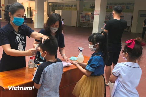 Học sinh được đo thân nhiệt và rửa tay bằng nước sát khuẩn trước khi vào lớp học. (Ảnh: Đức Duy/Vietnam+)
