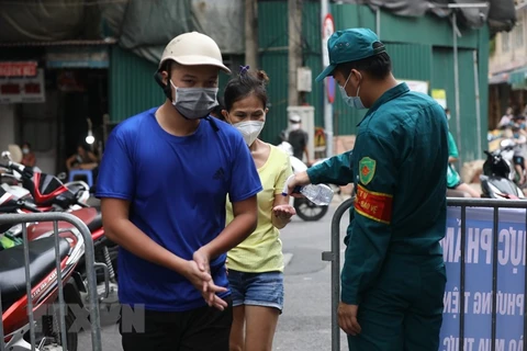 Lực lượng chức năng quận Hoàn Kiếm, kiểm soát, xịt sát khuẩn tay cho người vào chợ tại khu mua sắm hàng thiết yếu. (Ảnh: TTXVN)