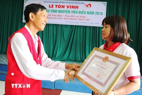 Chủ tịch Hội Chữ thập đỏ tỉnh An Giang Ngô Văn Sở (bìa trái) trao Bằng khen cho chị Phan Thị Mỹ Vân. (Ảnh: Vương Thoại Trung/TTXVN)