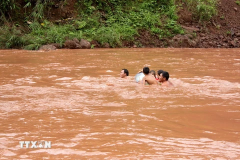Phụ huynh và giáo viên nguy hiểm vượt dòng nước dữ đưa học sinh qua suối đến trường. (Ảnh: Việt Hoàng/TTXVN)