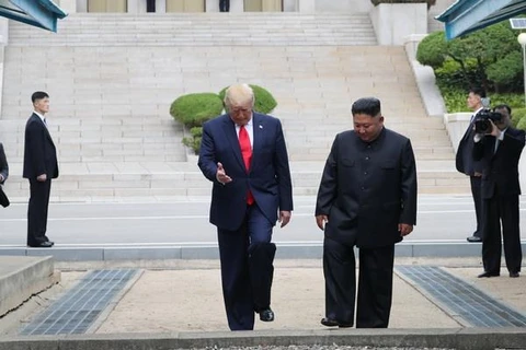 Tổng thống Mỹ Donald Trump (trái) và nhà lãnh đạo Triều Tiên Kim Jong-un bước chân qua đường ranh giới phân chia hai miền Triều Tiên tại DMZ, sang phần lãnh thổ của Triều Tiên chiều 30/6/2019. (Ảnh: AFP/TTXVN)