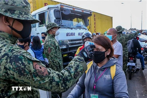 Cảnh sát kiểm tra thân nhiệt nhằm ngăn chặn sự lây lan của dịch COVID-19 tại một trạm kiểm soát ở Quezon, Philippines. (Nguồn: THX/TTXVN) 