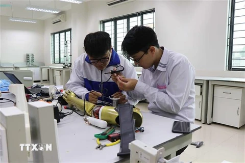 Phạm Đức Linh và Nguyễn Văn An cùng nhau nghiên cứu sản phẩm Cánh tay robot cho người khuyết tật liệt cơ tay toàn phần. (Ảnh: Thanh Thương/TTXVN) 