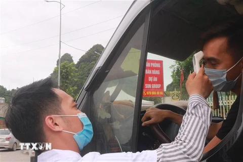 Nhân viên y tế kiểm tra thân nhiệt cho người dân khi ra, vào địa bàn thành phố Cẩm Phả (Quảng Ninh). (Ảnh: Thanh Vân/TTXVN) 