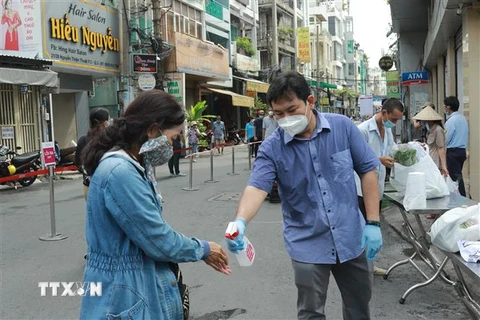 Người dân xịt tay sát khuẩn trước khi vào khu vực mua sắm của 'Phiên chợ lưu động' được tổ chức tại khu phố 3, phường 2, Quận 3, Thành phố Hồ Chí Minh. (Ảnh: Quang Châu/TTXVN) 