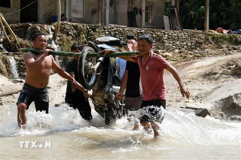 Người dân phải khiêng xe máy, đồ dùng qua cầu tràn do dòng nước chảy xiết. (Ảnh: Nam Thái/TTXVN) 