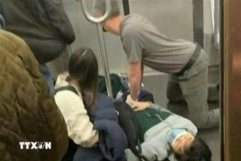 Hành khách sơ cứu cho một người bị thương sau vụ nổ súng trên tàu điện ngầm ở New York, Mỹ ngày 12/4/2022. (Ảnh: AFP/TTXVN)