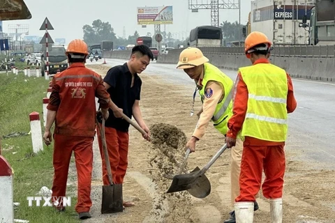 Cảnh sát Giao thông Nghệ An cùng người dân dùng cát, chổi để xử lý số dầu loang. (Ảnh: TTXVN phát)