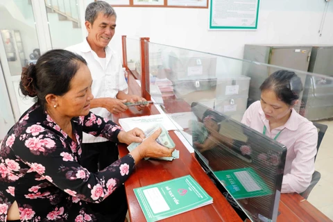 Vợ chồng ông Hoàng Hữu Hiện rất vui khi đến Ngân hàng CSXH huyện Lệ Thủy nhận 100 triệu đồng vốn vay để đầu tư nuôi lợn rừng, lợn nái. (Ảnh: Vietnam+)