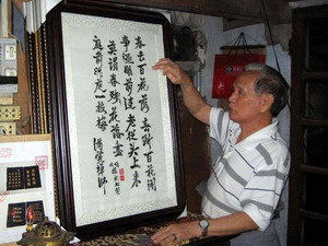 Nghệ nhân Lê Văn Kinh bên các bức tranh thêu bằng tiếng Việt và tiếng Hán (Trung Quốc). (Ảnh: Quốc Việt/TTXVN)