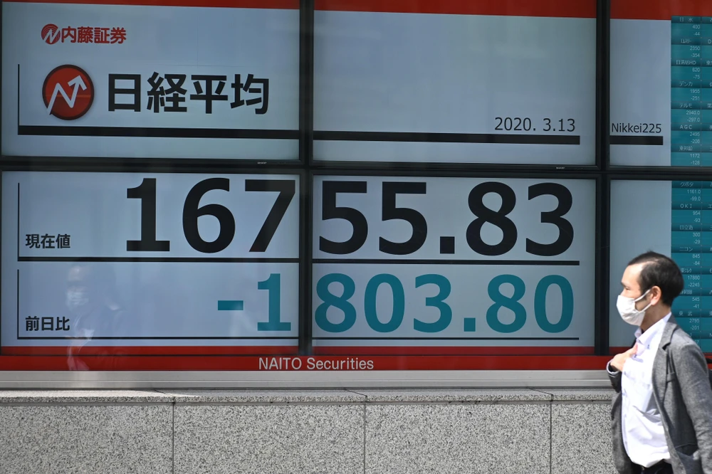 Người dân đeo khẩu trang phòng COVID-19 đi qua bảng điện tử tại Sở giao dịch chứng khoán Tokyo. (Nguồn: AFP)