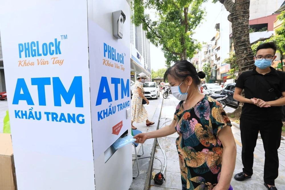 Người dân đến nhận khẩu trang từ cây ATM phát khẩu trang miễn phí trên phố Lạc Trung, Hà Nội. (Ảnh: Thành Đạt/TTXVN)