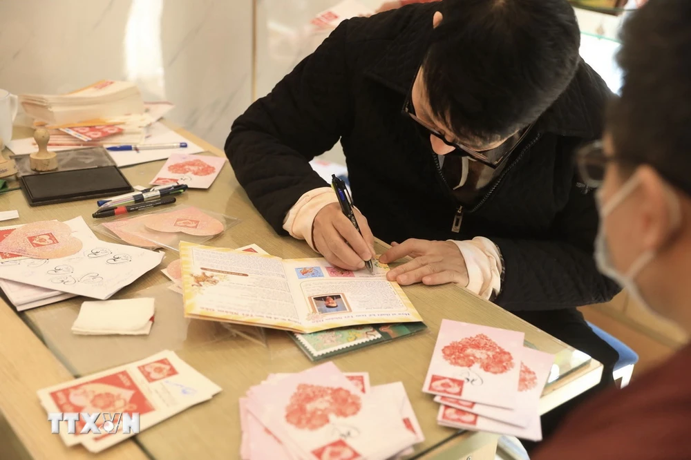 Hoạ sỹ Nguyễn Quang Vinh ký tặng người chơi tem trong dịp phát hành một bộ tem về tình yêu. (Ảnh: Minh Quyết/TTXVN)