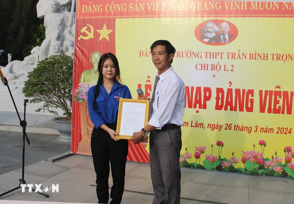 Đại diện Đảng ủy Trường Trung học Phổ thông Trần Bình Trọng, huyện Cam Lâm trao Quyết định kết nạp đảng viên cho quần chúng ưu tú Lâm Uyên Kha. (Ảnh: Phan Sáu/TTXVN)