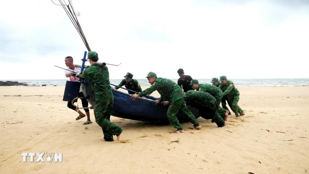 Cán bộ, chiến sỹ Đồn Biên phòng Lý Hòa (Bộ đội Biên phòng Quảng Bình) giúp ngư dân xã Đức Trạch, huyện Bố Trạch, tỉnh Quảng Bình đưa thuyền lên bờ tránh trú. (Ảnh: TTXVN phát)