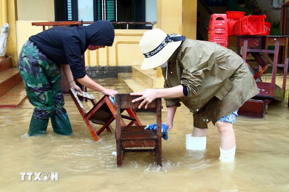 Giáo viên Trường Tiểu học Võ Ninh (huyện Quảng Ninh, Quảng Bình) tận dụng nước lũ để lau chùi bàn ghế khi nước lũ đang rút. (Ảnh: Tá Chuyên/TTXVN)