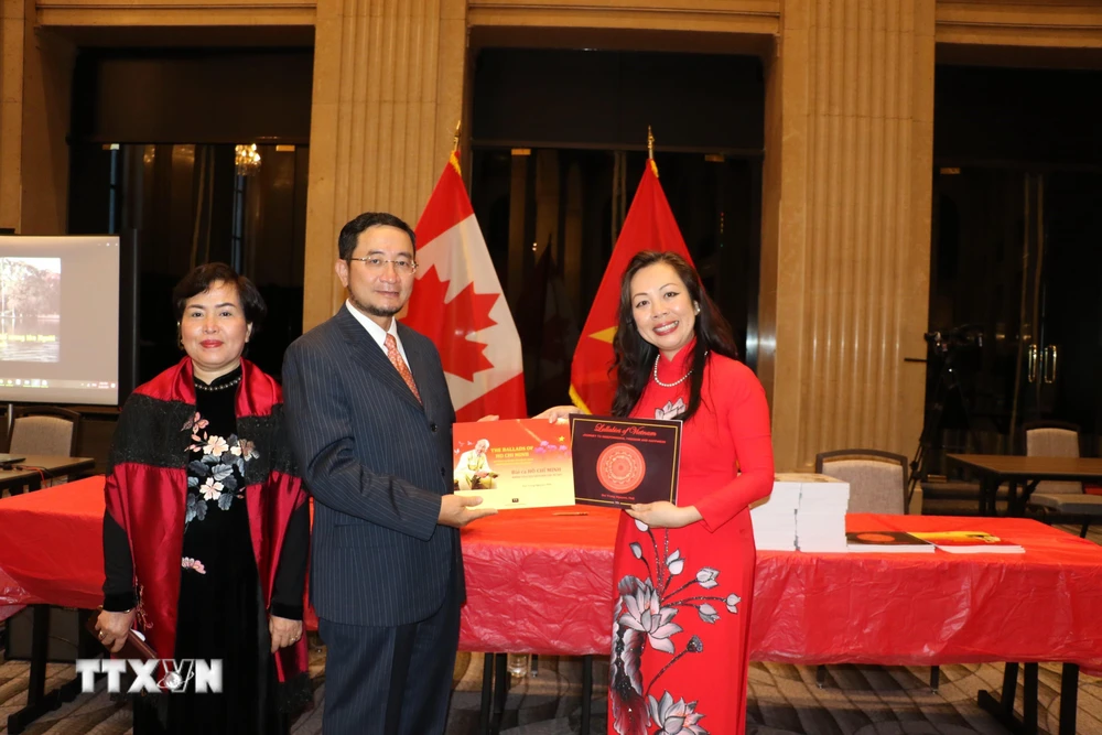 Giáo sư Julie Nguyễn (áo đỏ) tặng Đại sứ Việt Nam tại Canada Phạm Cao Phong và phu nhân hai tác phẩm "Bài ca Hồ Chí Minh" và "Lời ru nước Việt" mà giáo sư vừa ra mắt. (Ảnh: Vũ Quang Thịnh/TTXVN)