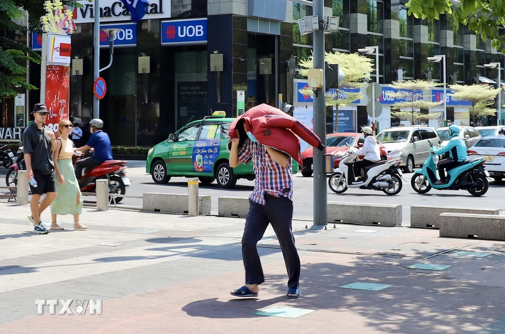 Một người dân tại Thành phố Hồ Chí Minh dùng áo che kín đầu, bước vội giữa trời nắng nóng. (Ảnh: Hồng Giang/TTXVN)