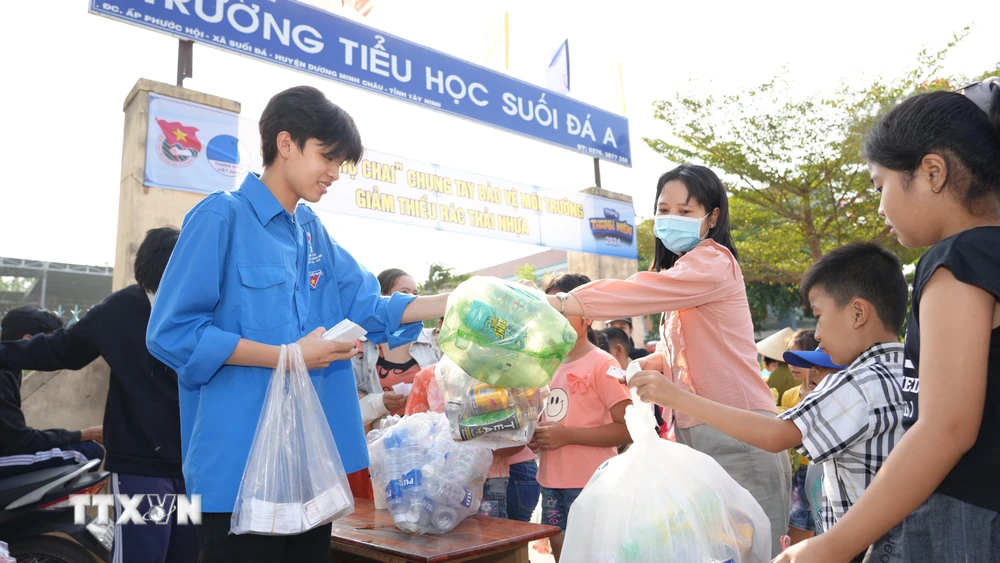 Đoàn viên Thanh niên xã Suối Đá thu gom chai nhựa sử dụng một lần và phát phiếu tham gia phiên chợ chai cho người dân. (Ảnh: Minh Phú/TTXVN)