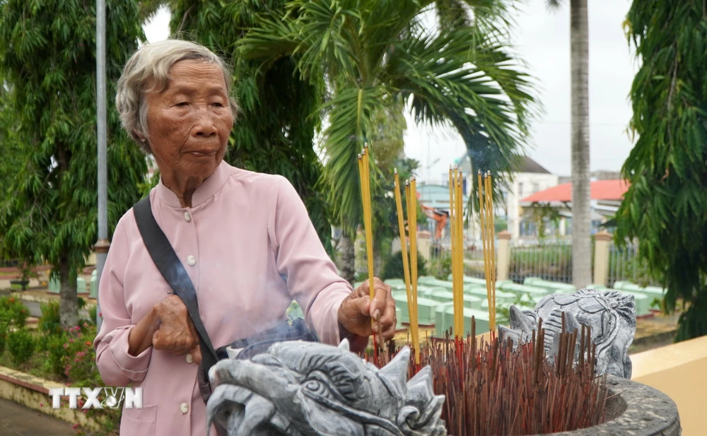 Bà Đặng Thị Bảy thắp hương cho đồng đội đang yên nghỉ tại Nghĩa trang liệt sĩ xã Long Hưng A. (Ảnh: Nhựt An/TTXVN)