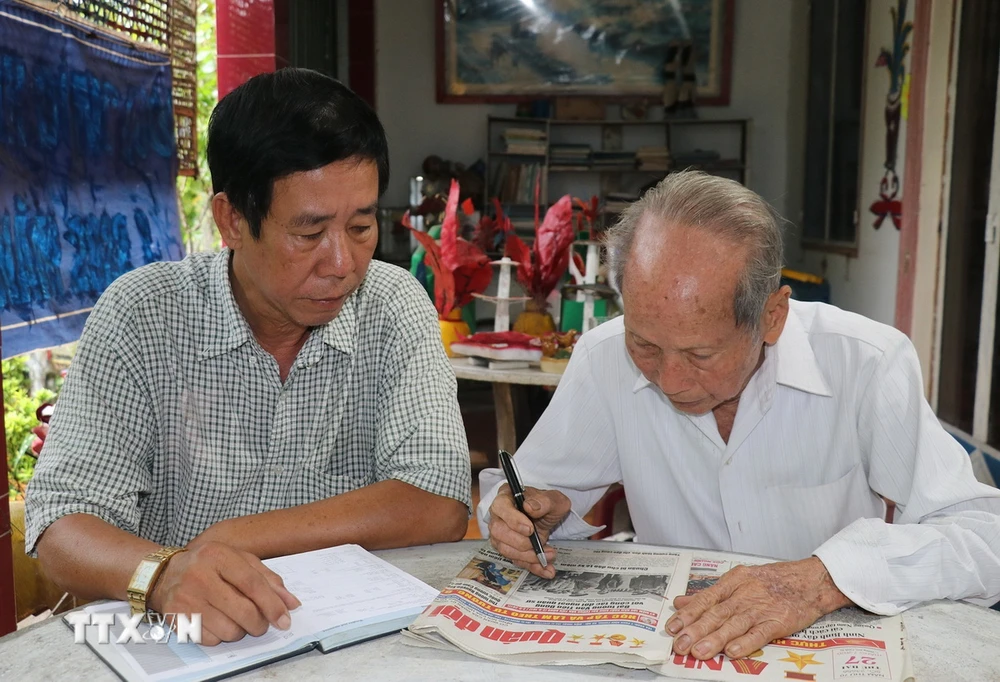 Ông Nguyễn Văn Thọ (phải) và con trai Nguyễn Thanh Hà đọc thông tin ở mục tìm thân nhân liệt sỹ trên báo. (Ảnh: Hữu Chí/TTXVN)