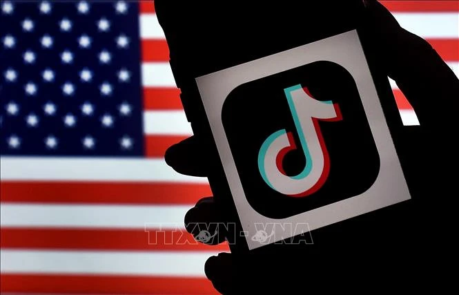 Biểu tượng ứng dụng TikTok trên màn hình điện thoại và quốc kỳ Mỹ (phía sau). (Ảnh: AFP/TTXVN)