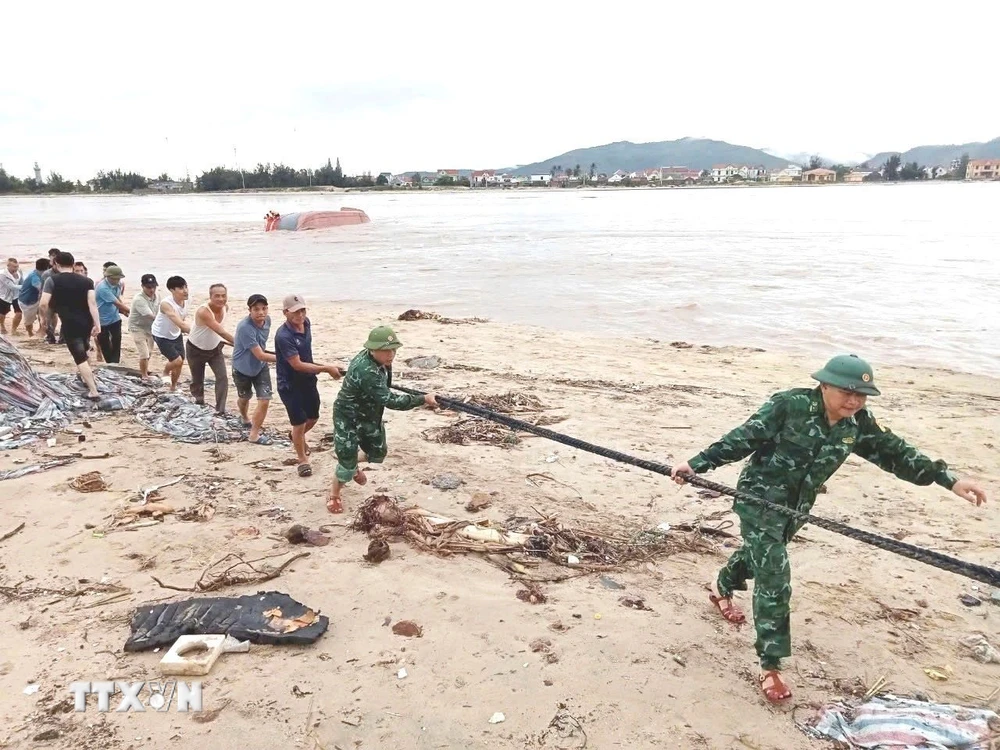 Cán bộ, chiến sỹ Đồn Biên phòng Cửa khẩu Cảng Gianh (Bộ đội Biên phòng Quảng Bình) và người dân cùng các lực lượng liên quan triển khai các biện pháp cứu hộ tàu cá bị lật. (Ảnh: TTXVN phát)