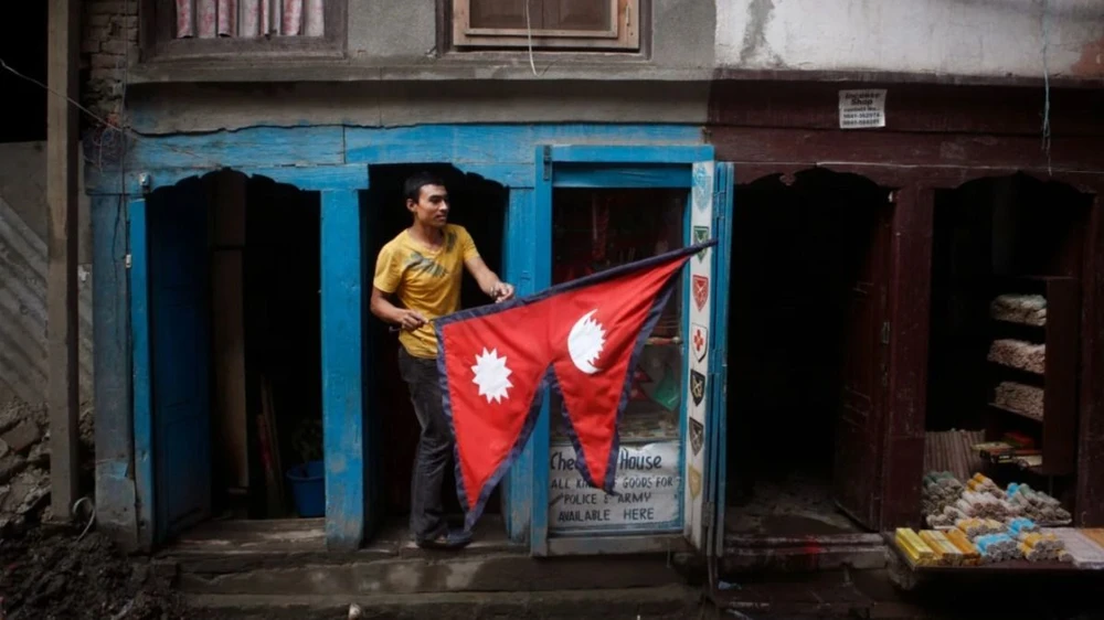 Một người dân cầm lá quốc kỳ Nepal bên ngoài quầy hàng của mình ở Kathmandu. (Nguồn: AP/CNN)