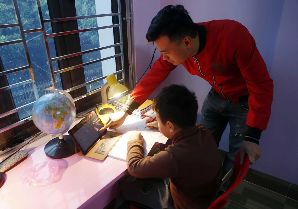 Phụ huynh hỗ trợ học sinh lớp 3 trường Tiểu học Hoàng Lê, thành phố Hưng Yên học trực tuyến tại nhà. (Ảnh: Phạm Kiên/TTXVN)