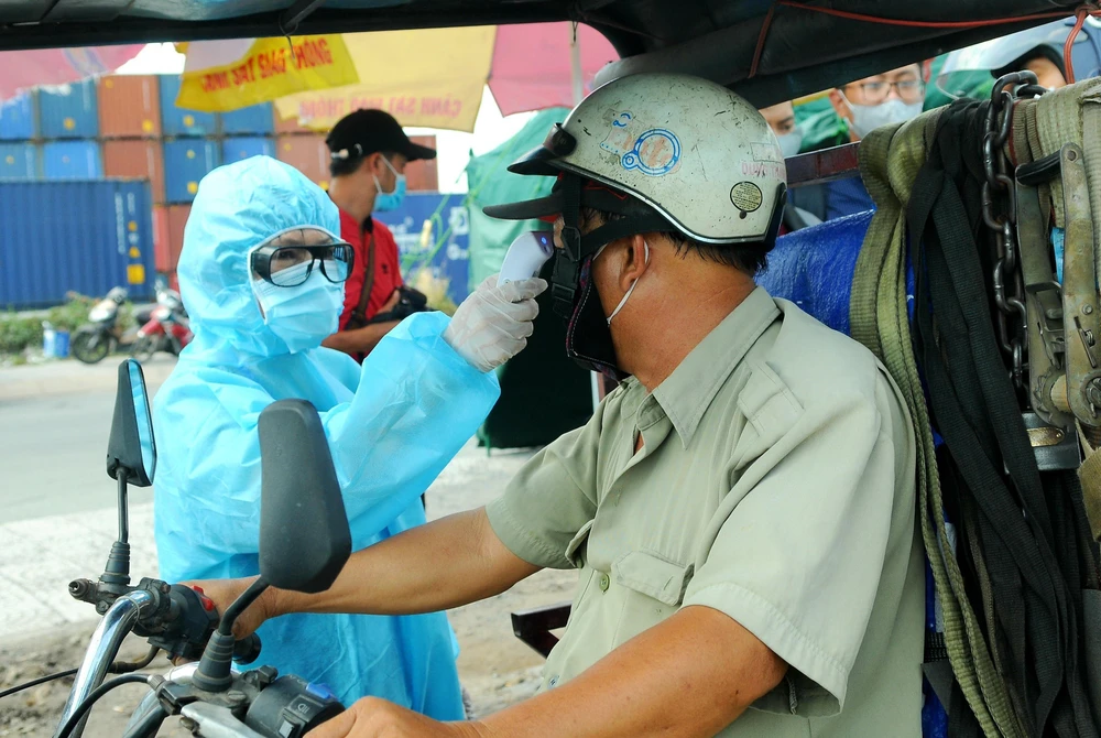 Nhân viên y tế đo thân nhiệt người ra vào Thành phố Hồ Chí Minh tại chốt kiểm dịch. (Ảnh: Đinh Hằng/TTXVN)