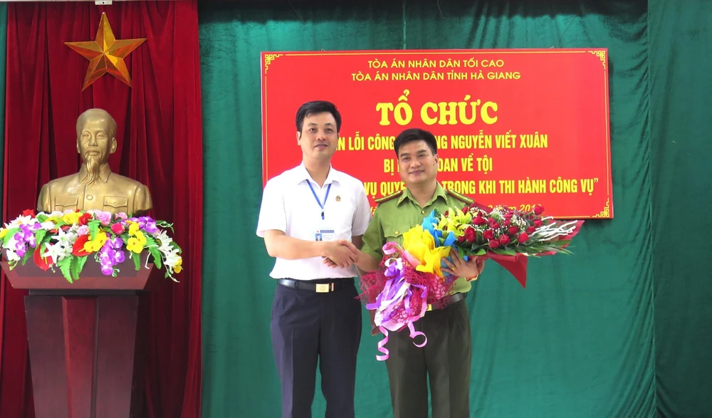 Phó Chánh án TAND tỉnh Hà Giang Trương Huy Huân tặng hoa cho ông Nguyễn Viết Xuân. (Ảnh: Minh Tâm-TTXVN)