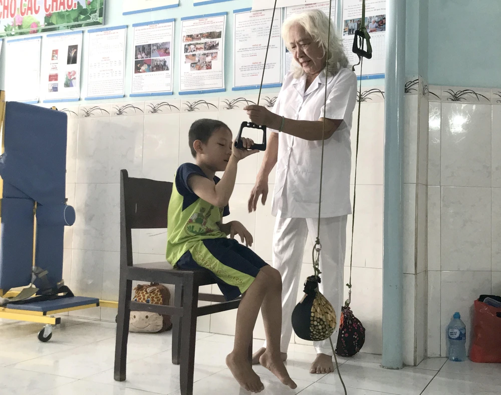 Bà Nguyễn Ngọc Điểu tập luyện phục hồi chức năng vận động cho bé Phan Thanh Phong. (Ảnh: Lê Thúy Hằng/TTXVN)