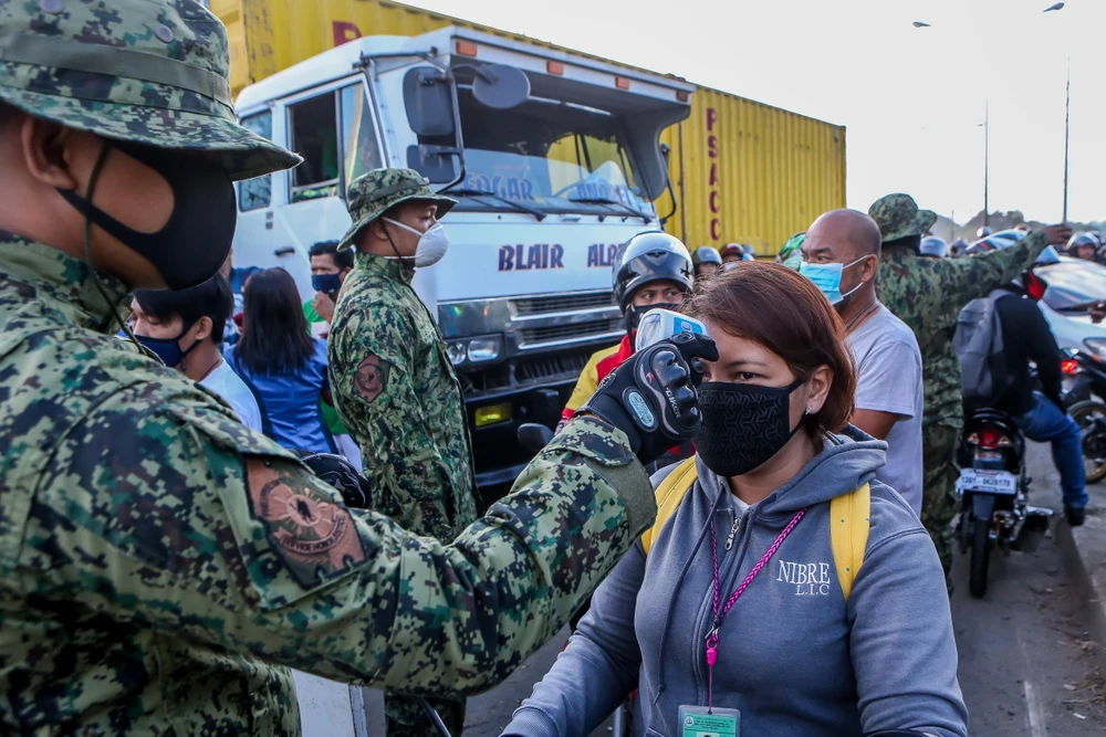 Cảnh sát kiểm tra thân nhiệt nhằm ngăn chặn sự lây lan của dịch COVID-19 tại một trạm kiểm soát ở Quezon, Philippines. (Ảnh: THX/TTXVN)
