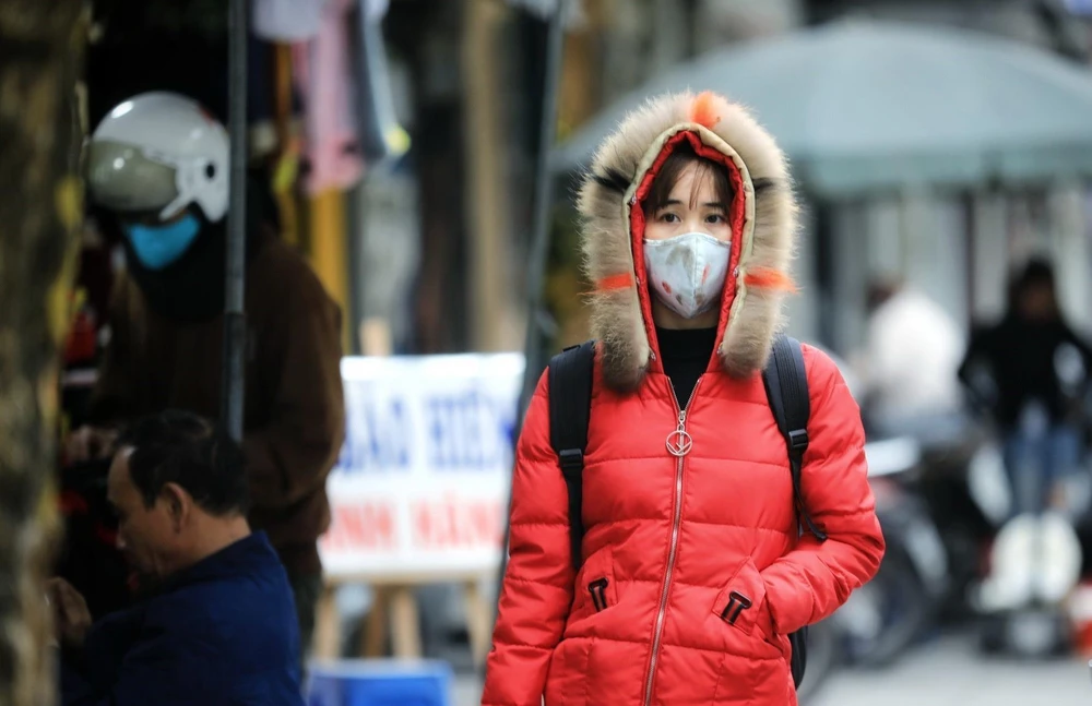 Người dân ra đường đều mặc áo ấm kín mít, đeo khẩu trang để chống lại cơn gió lạnh đầu mùa. (Ảnh: Thành Đạt/TTXVN)