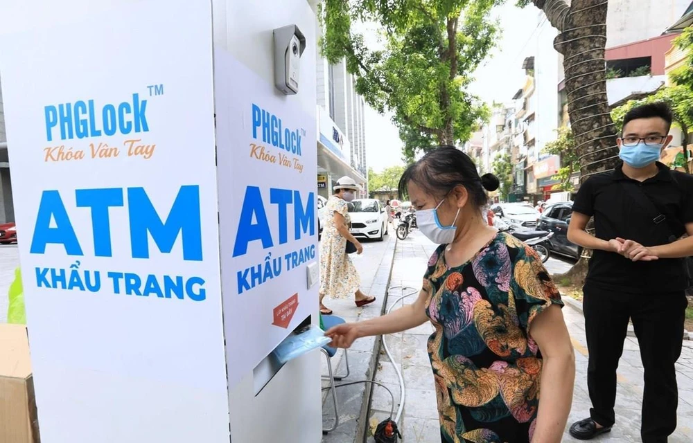 Người dân đến nhận khẩu trang từ cây ATM phát khẩu trang miễn phí trên phố Lạc Trung, Hà Nội. (Ảnh: Thành Đạt/TTXVN)