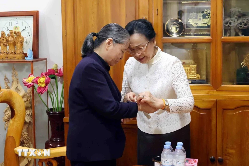 Bà Naly Sisoulith, Phu nhân Tổng Bí thư, Chủ tịch nước Lào Thongloun Sisoulith buộc chỉ cổ tay chúc may mắn, bình an tới bà Ngô Thị Mận, Phu nhân cố Tổng Bí thư Nguyễn Phú Trọng. (Ảnh: Phạm Kiên/TTXVN)