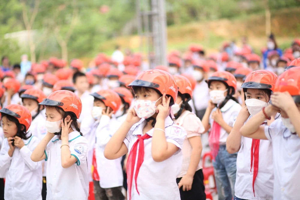 Hướng dẫn học sinh tiểu học đội mũ bảo hiểm khi tham gia giao thông. (Ảnh: PV/Vietnam+)