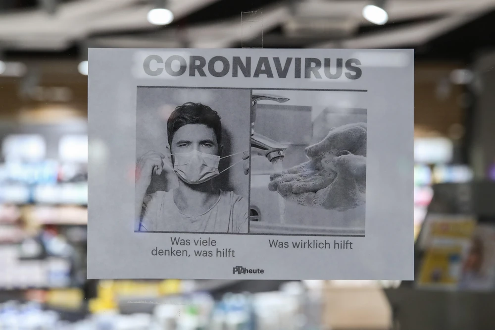 Tấm biển kêu gọi người dân rửa tay thường xuyên và đeo khẩu trang để phòng tránh lây nhiễm COVID-19, tại một hiệu thuốc ở Berlin, Đức (Ảnh: THX/TTXVN)