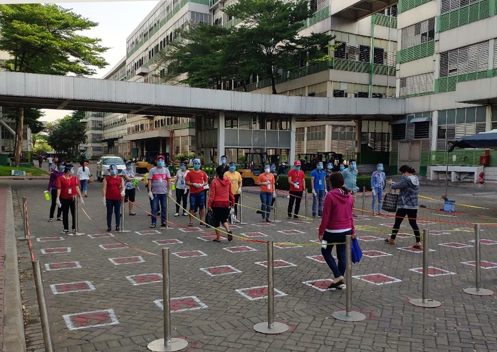 Công nhân Công ty TNHH Pouyuen Việt Nam thực hiện giãn ca, rửa tay khử trùng và đo thân nhiệt trước khi vào xưởng. (Ảnh: Thanh Vũ/TTXVN)