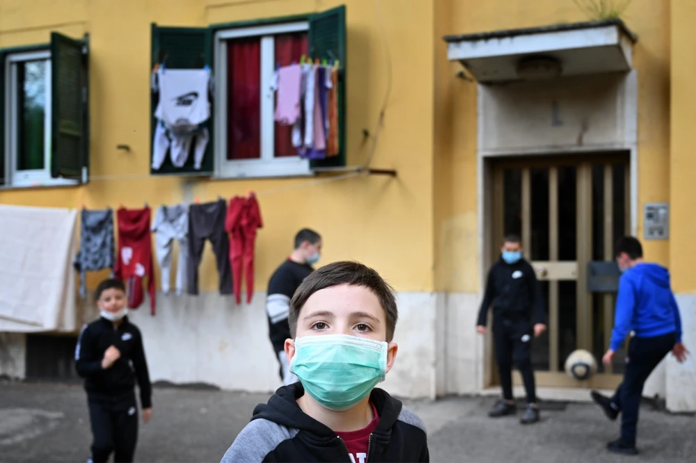Trẻ em đeo khẩu trang khi chơi trước cửa nhà ở San Basilio, Rome, Italy ngày 18/4/2020 trong bối cảnh dịch COVID-19 đang hoành hành. (Ảnh: AFP/TTXVN)