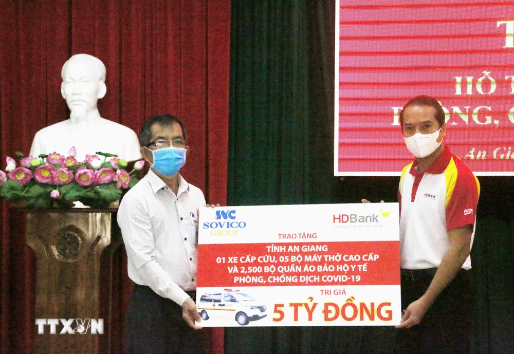 Đại diện Tập đoàn Sovico và Ngân hàng Thương mại Cổ phần Phát triển Thành phố Hồ Chí Minh HDBank (phải) trao bảng tượng trưng tăng tỉnh An Giang 1 xe cấp cứu, 5 máy thở cao cấp, 2.500 bộ quần áo bảo hộ y tế. (Ảnh: Công Mạo/TTXVN)