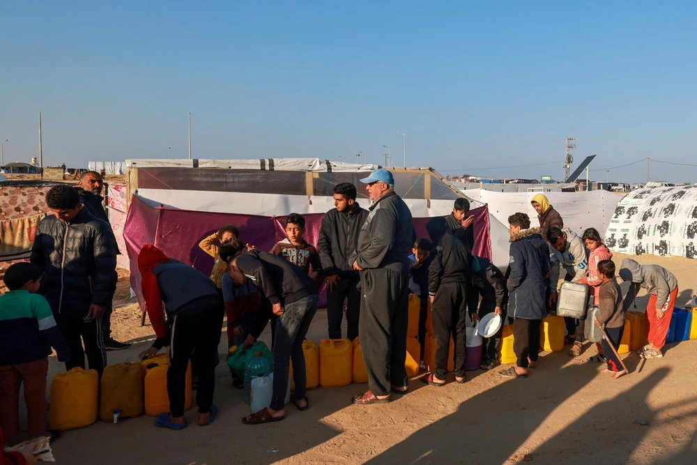 Người Palestine xếp hàng lấy nước sinh hoạt tại khu lều tạm ở Dải Gaza, ngày 16/1/2024. (Ảnh: AFP/TTXVN)
