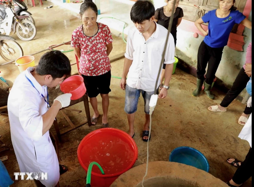 Nhân viên y tế dự phòng hướng dẫn người dân khử khuẩn nước sinh hoạt bằng dung dịch Cloramin B. (Ảnh: Vũ Sinh/TTXVN)