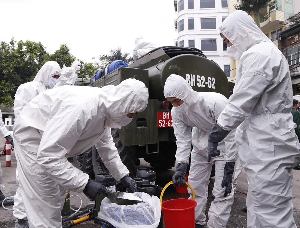 Lực lượng hóa học pha hóa chất để tiến hành phun tiêu tẩy khu vực phố Trúc Bạch, quận Ba Đình. (Ảnh: Dương Giang/TTXVN)